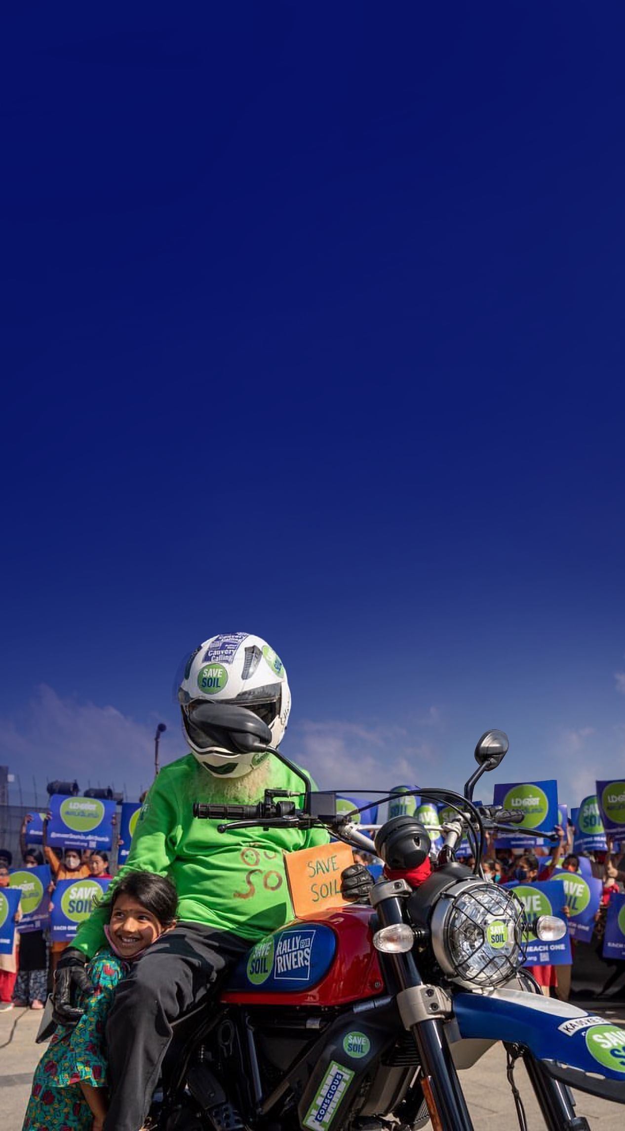 Sadhguru pe motocicletă cu semnul Salvează Solul, alături de un copil