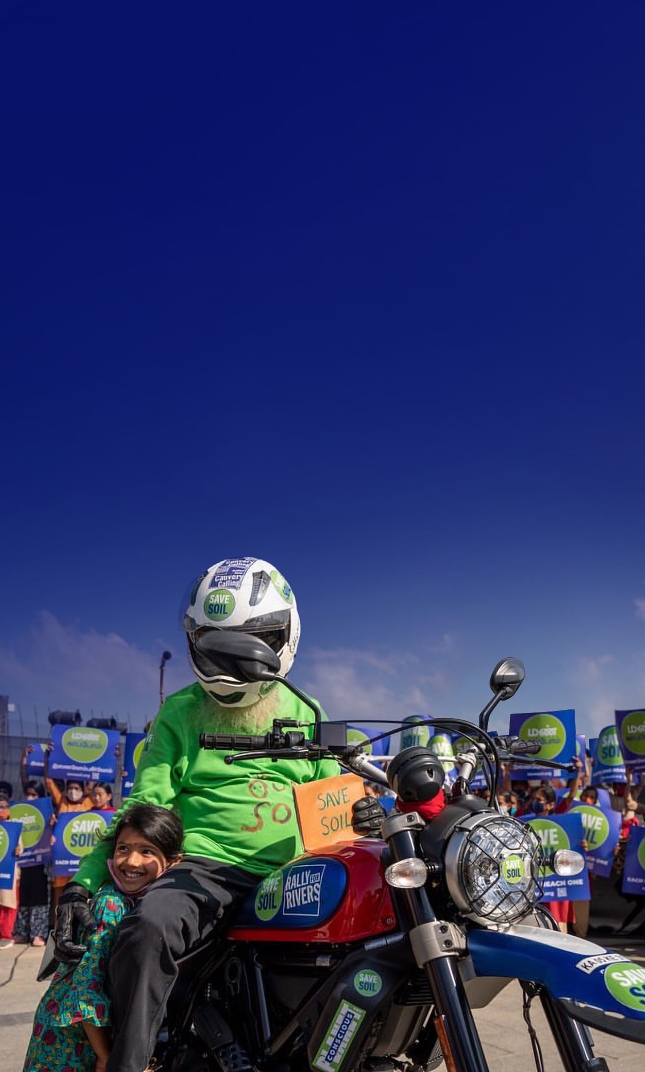 Sadhguru de moto com o cartaz Salve o Solo, junto a uma criança